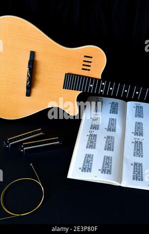 Un plat musical se pose sur fond noir, avec une guitare acoustique en bois, des harmonicas et un livre de tablature. Banque D'Images