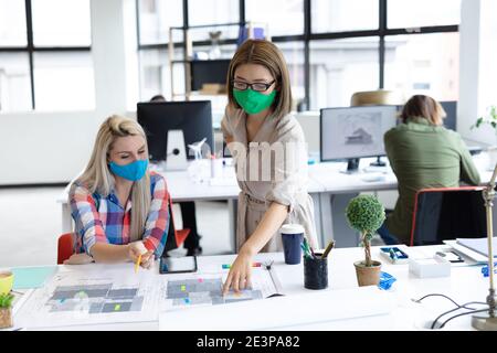 Deux femmes d'affaires diverses portant des masques de visage regardant les plans et discussion Banque D'Images