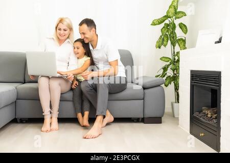 Famille heureuse avec une fille gamin s'amusant en utilisant un ordinateur portable ensemble assis sur un canapé, parents et fille enfant riant se détendre à la maison avec un ordinateur Banque D'Images