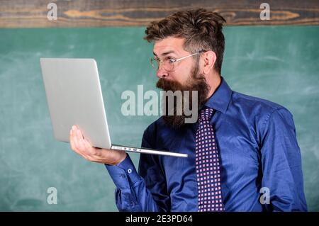 Hipster professeur porter lunettes et cravate tient ordinateur portable surfer sur Internet. Des nouvelles choquantes. Professeur barbu homme choqué avec ordinateur portable moderne surfer sur Internet tableau noir fond. Des informations choquantes. Banque D'Images