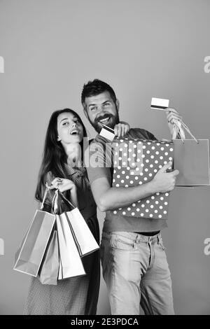Couple amoureux tient des sacs de shopping sur fond rose. Un homme avec une barbe tient une carte de crédit et une boîte à pois. Shopping et loisirs. Un gars avec la barbe et une fille avec des visages souriants font du shopping. Banque D'Images