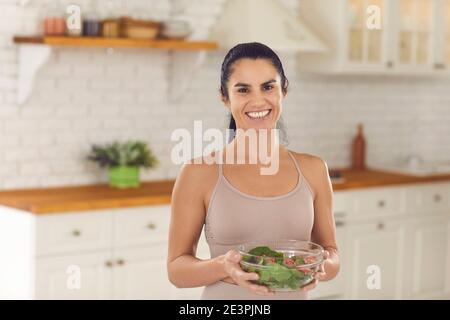 Portrait d'une femme mince en sport top tenant bol de salade de légumes et sourire à l'appareil photo Banque D'Images