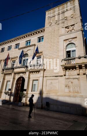 Silhouette d'homme avec bâton de marche contre un bâtiment historique qui abrite maintenant des bureaux du gouvernement, la place du peuple, Zadar, Dalmatie, Croatie Banque D'Images