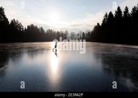 Silhouette d'un jeune patinage sur glace sur un lac gelé, éclairé par le soleil depuis le dos au lever du soleil, en Slovénie Banque D'Images