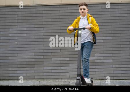 Adolescent moderne avec sac à dos sur scooter électrique sur brique arrière-plan de la paroi Banque D'Images