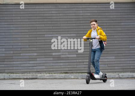 Adolescent moderne avec sac à dos sur scooter électrique sur brique arrière-plan de la paroi Banque D'Images