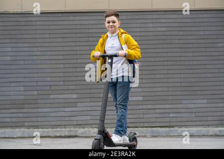 Adolescent moderne avec sac à dos sur scooter électrique sur brique arrière-plan de la paroi Banque D'Images