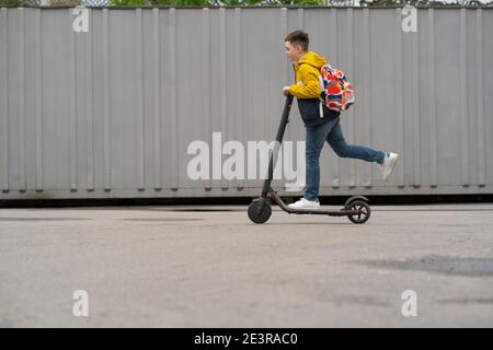 Adolescent moderne avec des promenades à dos sur scooter électrique. Le garçon revient de l'école Banque D'Images