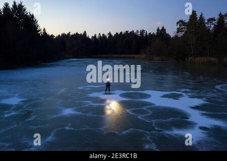 Femme avec un phare debout sur un lac gelé au crépuscule Banque D'Images