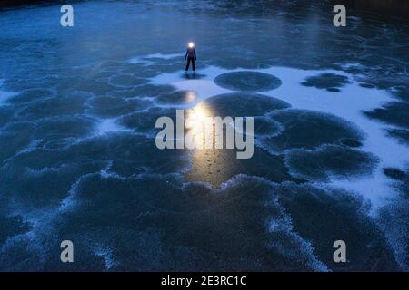 Femme avec un phare debout sur un lac gelé au crépuscule Banque D'Images