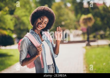 Photo portrait de la jolie fille à la peau noire avec des cheveux bouclés salutation souriante en branle main gardant sac à dos portant une tenue en denim Banque D'Images