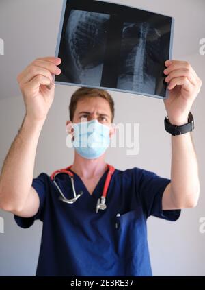 un beau médecin hommes portant un gommage, un stéthoscope et un masque facial regardant une radiographie pendant la pandémie de cov 2 du sras covid 19 Banque D'Images