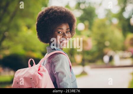 Vue de derrière photo portrait d'une étudiante à la peau noire marche dans le parc porter un jean décontracté chemise rose sac à dos sourire Banque D'Images