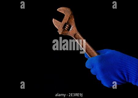 La main d'un homme dans un gant bleu tient une clé rouillée. Gros plan Banque D'Images