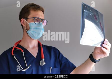 un beau médecin hommes portant un gommage, un stéthoscope et un masque facial regardant une radiographie pendant la pandémie de cov 2 du sras covid 19 Banque D'Images
