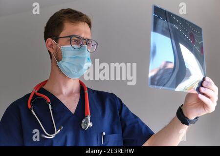 un beau médecin hommes portant un gommage, un stéthoscope et un masque facial regardant une radiographie pendant la pandémie de cov 2 du sras covid 19 Banque D'Images