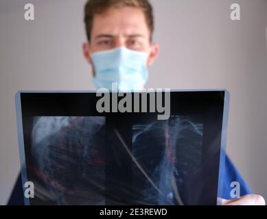 un beau médecin hommes portant un gommage, un stéthoscope et un masque facial regardant une radiographie pendant la pandémie de cov 2 du sras covid 19 Banque D'Images
