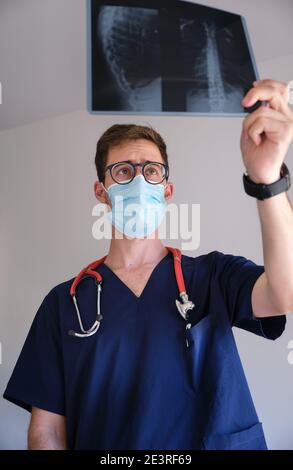 un beau médecin hommes portant un gommage, un stéthoscope et un masque facial regardant une radiographie pendant la pandémie de cov 2 du sras covid 19 Banque D'Images