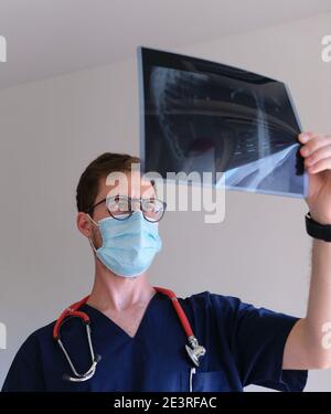 un beau médecin hommes portant un gommage, un stéthoscope et un masque facial regardant une radiographie pendant la pandémie de cov 2 du sras covid 19 Banque D'Images