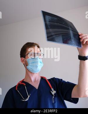 un beau médecin hommes portant un gommage, un stéthoscope et un masque facial regardant une radiographie pendant la pandémie de cov 2 du sras covid 19 Banque D'Images