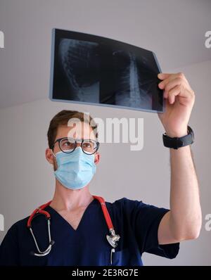 un beau médecin hommes portant un gommage, un stéthoscope et un masque facial regardant une radiographie pendant la pandémie de cov 2 du sras covid 19 Banque D'Images