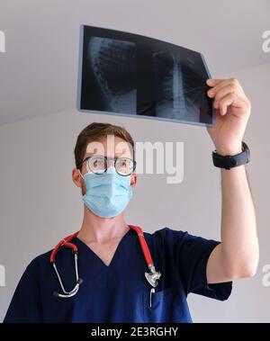un beau médecin hommes portant un gommage, un stéthoscope et un masque facial regardant une radiographie pendant la pandémie de cov 2 du sras covid 19 Banque D'Images