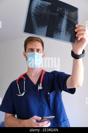 un beau médecin hommes portant un gommage, un stéthoscope et un masque facial regardant une radiographie pendant la pandémie de cov 2 du sras covid 19 Banque D'Images