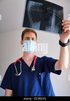 un beau médecin hommes portant un gommage, un stéthoscope et un masque facial regardant une radiographie pendant la pandémie de cov 2 du sras covid 19 Banque D'Images