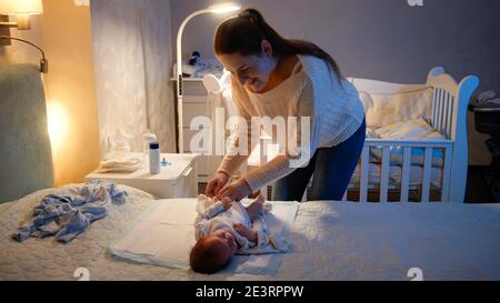 Une jeune mère qui s'occupe de lui habille son petit bébé la nuit. Parent mettant des vêtements sur un nouveau-né. Concept de parents aimant et attentionné, nouveau-né Banque D'Images