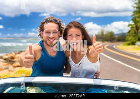 Voiture bon voyage les jeunes conducteurs conduisant dans une voiture cabriolet cabriolet. Un couple souriant fait le pouce sur la route des vacances d'été en voiture neuve Banque D'Images