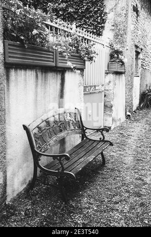 Paisible rue de village dans la campagne française. Banc en bois avec décoration de raisin forgée près du mur de jardin. Photo en noir et blanc. Banque D'Images