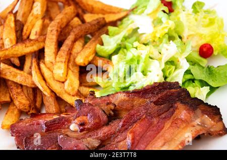 Poitrine de porc grillée, frites et salade verte. Repas traditionnel simple Banque D'Images