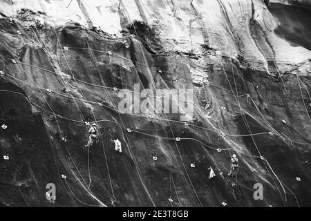Les travailleurs renforcent la pente de la montagne avec un maillage métallique empêchant la chute sur la route.Hondarribia, Espagne.Photo historique noir blanc. Banque D'Images