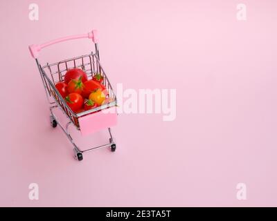 Chariot d'épicerie rose plein de tomates sur fond rose Banque D'Images