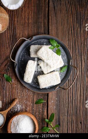 Délicieux dessert sucré, lamingtons au chocolat blanc recouverts de noix de coco râpée sur fond rustique en bois Banque D'Images