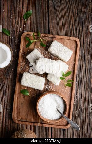 Délicieux dessert sucré, lamingtons au chocolat blanc recouverts de noix de coco râpée sur fond rustique en bois Banque D'Images