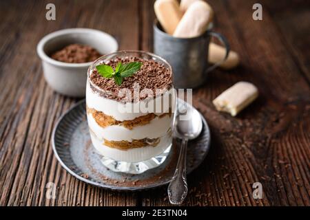 Café italien classique, dessert sans cuisson, délicieux Tiramisu facile dans un pot, arrosé de poudre de cacao et de copeaux de chocolat sur un backgrou rustique en bois Banque D'Images
