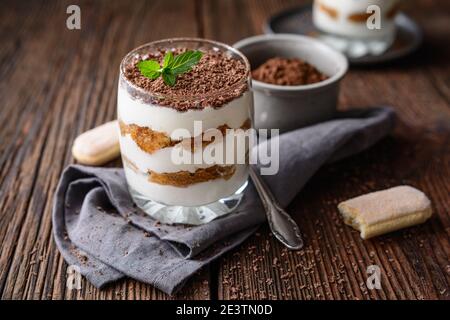 Café italien classique, dessert sans cuisson, délicieux Tiramisu facile dans un pot, arrosé de poudre de cacao et de copeaux de chocolat sur un backgrou rustique en bois Banque D'Images