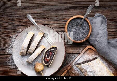 Délicieux dessert roulé, pâte feuilletée de graines de pavot aux tranches de strudel à la cerise aigre, saupoudrés de sucre sur fond de bois rustique Banque D'Images