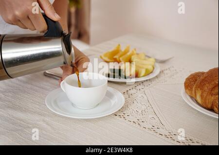 Gros plan portrait d'une femme qui verse du café d'une cafetière geyser dans une tasse blanche sur la table. Banque D'Images