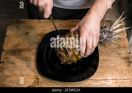 L'homme coupe l'ananas avec un couteau sur une table en bois Banque D'Images
