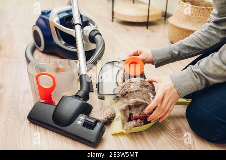 La femme au foyer retire les déchets et les cheveux de chat du filtre à poussière de l'aspirateur à la maison. Récipient plein de saleté. Banque D'Images