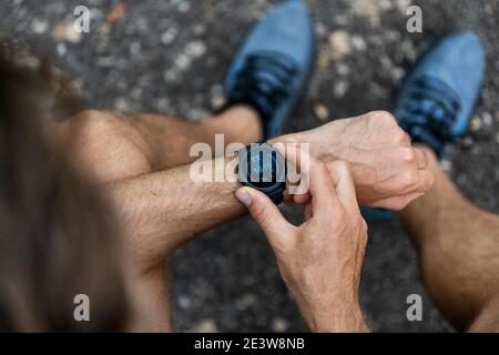 FIT homme vérifiant la montre intelligente technologie wearable montre sport SmartWatch sur la course de forme physique à l'extérieur. Vue de dessus avec des chaussures de course dans la rue. Banque D'Images