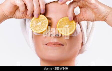 Un portrait agrandi d'une femme âgée caucasie avec des tranches de citron devant ses yeux sur fond blanc. Le Skinimalisme et la peau saine senior Banque D'Images