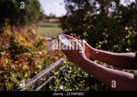 Un garçon noir est en train de lire tous les e-mails non lus sur son smartphone pendant une journée ensoleillée incroyable, dans un jardin Banque D'Images