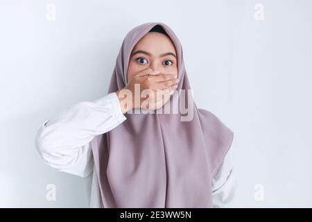 La jeune femme asiatique de l'Islam portant un foulard est choquée avec ses mains couvrant sa bouche. Femme indonésienne sur fond gris. Banque D'Images