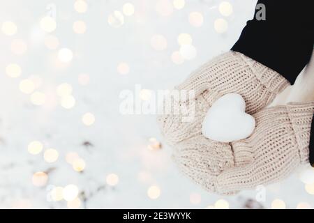 Boule de neige coeur dans les mains gantées de fille. Arrière-plan flou Banque D'Images