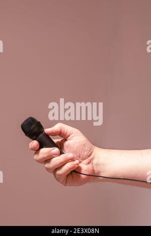 Main d'un homme tenant un microphone noir. Concept de communication, entretiens, dialogues virtuels. Banque D'Images