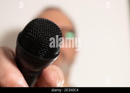 Main d'un homme tenant un microphone noir. Concept de communication, entretiens, dialogues virtuels. Banque D'Images