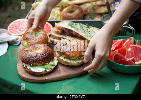 Mains atteignant pour des sandwichs bagels avec fromage à la crème et avocat lors d'un brunch pique-nique en plein air Banque D'Images
